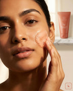 Woman applying a Sanatlyn Berries & Vitamin C Face Wash to her face with a bottle of the same product in the background.