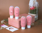 Pink skincare products with white caps on a wooden stand against a brown background