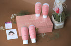 Set of pink skincare products with a decorative box on a brown surface.